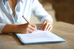 Close up of woman hands signing paper contract on table at home or office