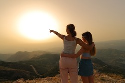 Two women pointing at sun at sunset in the mountain
