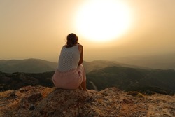 Back view portrait of a woman alone contemplating sunset in the mountain