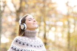 Relaxed woman listening to music and breathing fresh air in autumn in a forest or park