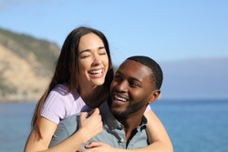 Happy interracial couple or friends laughing on piggyback on the beach