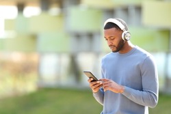 Black man walking checking music on smart phone in the street