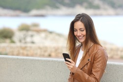 Happy woman using a smart phone on the beach with copy space and the sea in the background