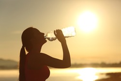 Profile of a fitness woman silhouette drinking water from a bottle at sunset with the sun in the background