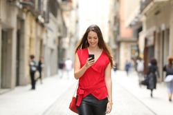 Front view of a fashion happy woman walking and using a smart phone on a city street