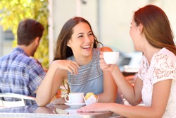 Two friends or sisters talking taking a conversation in a coffee shop terrace looking each other