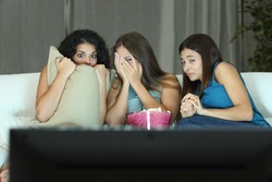 Girls watching a terror movie on tv sitting on a couch at home
