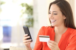 Lady buying online with a credit card and smart phone sitting on a couch at home with a blurred background