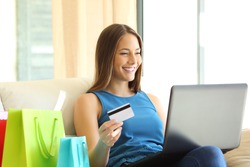 On line buyer shopping on line with credit card and a laptop sitting on a sofa with shopping bags beside at home