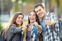 Three happy students looking at you with thumbs up in an university campus
