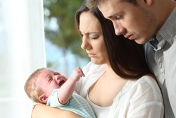 Tired desperate parents holding their baby crying desperately at home