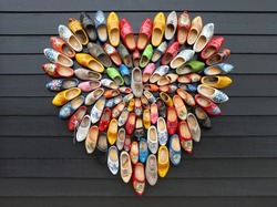 Many multicolored vintage Dutch Klomp shoes are laid out in the shape of a heart on black wood panel background