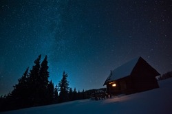 Majestic Milky Way over the winter mountains landscape. Night scene. Wooden house with light in window. Kukul ridge, Carpathians, Ukraine, Europe.