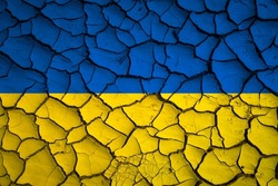 Ukraine national blue and yellow flag on a mud texture of dry cracks on the ground