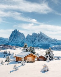 Picturesque landscape with small wooden log cabin on meadow Alpe di Siusi on sunrise time. Seiser Alm, Dolomites, Italy. Snowy hills with orange larch and Sassolungo and Langkofel mountains group