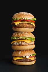 stack of different burgers on black background
