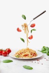 pasta with tomatoes and basil on a white background. Fork with pasta flying on a white background with tomatoes