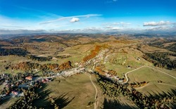 Boundless highlands covered with green coniferous and terracotta deciduous forests under cloudy sky on sunny autumn day aerial view