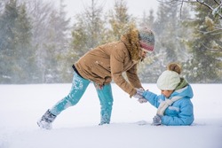 Back view of playful kids outerwear running, chasing in snowy spruce forest. Happy, cute female children playing catch, having fun outdoors in winter mountains. Concept of winter holidays.