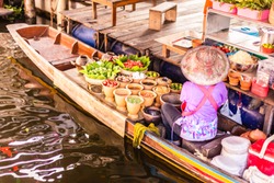 An unrecognizable Thai food peddler selling fruit and vegetables on her boat in the Damnoen Saduak floating market