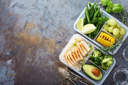 Healthy green meal prep containers with chicken, rice, avocado and vegetables overhead shot with copy space
