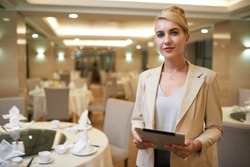 Pretty smiling wedding planner with tablet computer in restaurant