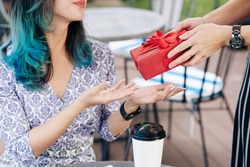 Cropped image of young woman accepting birthday present from friend when sitting at cafe table