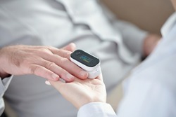 Close-up image of doctor measuring oxygen saturation of patient with pulse oximeter device