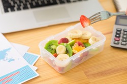 Plastic container with fruit salad and a fork on the desk, selective focus
