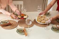 Hands of women putting plate with traditional snacks on table for Lunar New Year dinner party