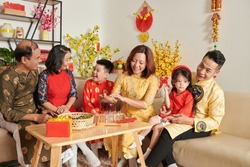 Three generation family celebrating Tet at home, talking and enjoying tea with candied fruits