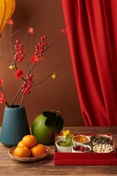 Fresh fruits, nuts and candied berries on table decorated with blooming peach branches for Chinese New Year celebration