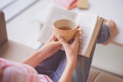Close-up of female hands holding teacup in front of opened book