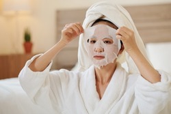 Asian young woman taking off sheet mask that immediately diminishing signs of agning