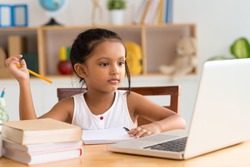 Little Indian girl looking at the laptop while doing homework
