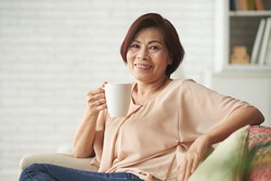 Portrait of happy mature Vietnamese woman with big mug of coffee