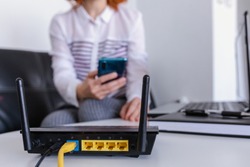 closeup of a wifi router and a redhead woman using smartphone on living room at home ofiice