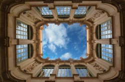 Bottom wide angle view of historic inner courtyard with beautiful facade building complex with blue sky and clouds and reflection in windows in Barcelona, Spain. Geometric shape