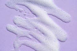 Foam swatch on a lilac background. Soapy liquid texture with bubbles. Natural sunshine and shadows. Skin care cleansing cosmetic in top view.