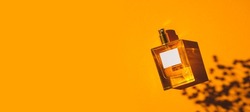 Transparent bottle of perfume on an orange background. Fragrance presentation with daylight. Trending concept in natural materials with plant shadow. Women's and men's essence.
