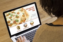 ordering food online concept: woman with a laptop showing fast food website on screen. Screen graphics are made up.
