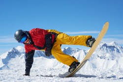 Snowboarder in bright sportswear doing balance trick against of beautiful mountains