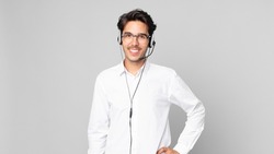 young hispanic man smiling happily with a hand on hip and confident. telemarketer concept