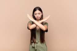 asian young woman looking annoyed and sick of your attitude, saying enough! hands crossed up front, telling you to stop
