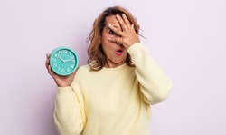 pretty middle age woman looking shocked, scared or terrified, covering face with hand. alarm clock concept