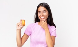 young hispanic woman smiling with a happy, confident expression with hand on chin and holding batteries