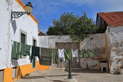 Laundry of military clothing drying in the sun and hanging from a wall-attached clothesline with holding up prop leaning on a green old fountain in Rua Antonio Maria Laboia Str. Faro-Algarve-Portugal.