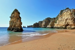 Sea stack rock formation on Praia de Dona Ana Beach southernmost end at the foot of the golden limestone and red clay cliffs that constitute the background of the sandy area. Lagos-Algarve-Portugal.