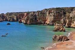 Sea stack rock formation on Praia de Dona Ana Beach southernmost end at the foot of the golden limestone and red clay cliffs that constitute the background of the sandy area. Lagos-Algarve-Portugal.