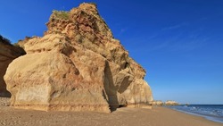 Tall pinnacle protruding from a rock formation on the golden sand detached from the nearby cliff that shelters Praia dos Tres Castelos-Three Castles Beach on its north side. Portimao-Algarve-Portugal.